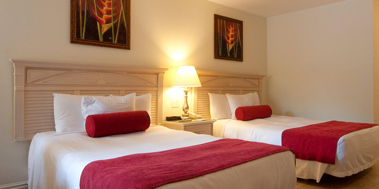 A hotel room with two neatly made beds, red throws, lamps, and wall art above the headboards.