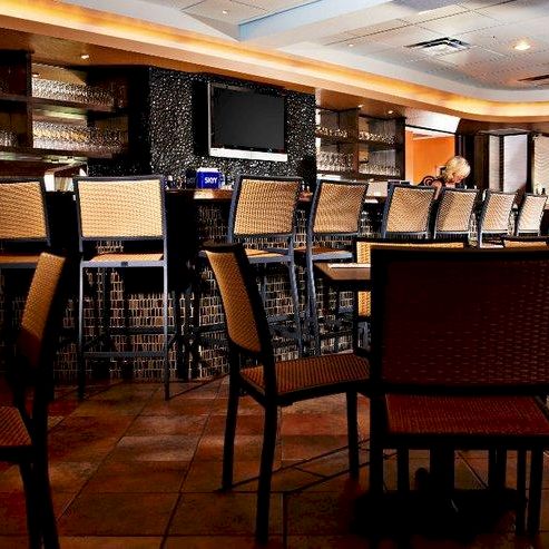 A cozy indoor bar or restaurant lounge with rows of woven chairs and a man seated in the background, under warm lighting.