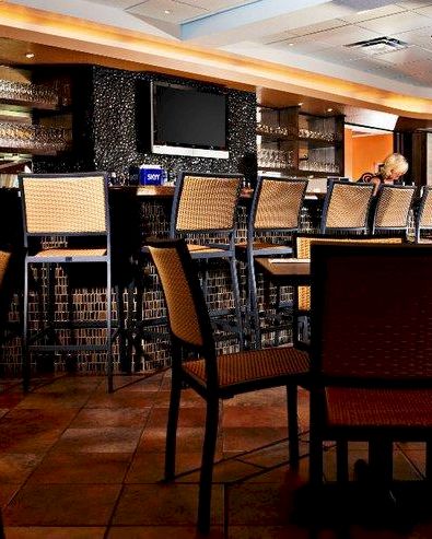 A cozy indoor bar or restaurant lounge with rows of woven chairs and a man seated in the background, under warm lighting.