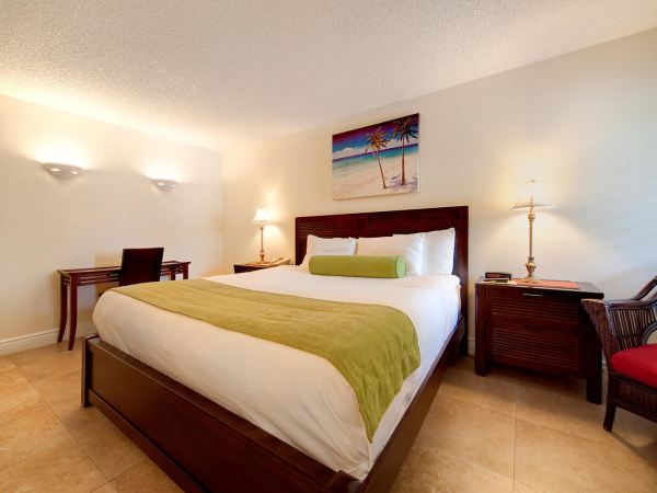 A tidy hotel bedroom with a king bed, nightstands, lamps, and a beach-themed wall painting.
