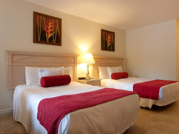 A hotel room with two beds, red blankets, bedside lamp, and two wall paintings.