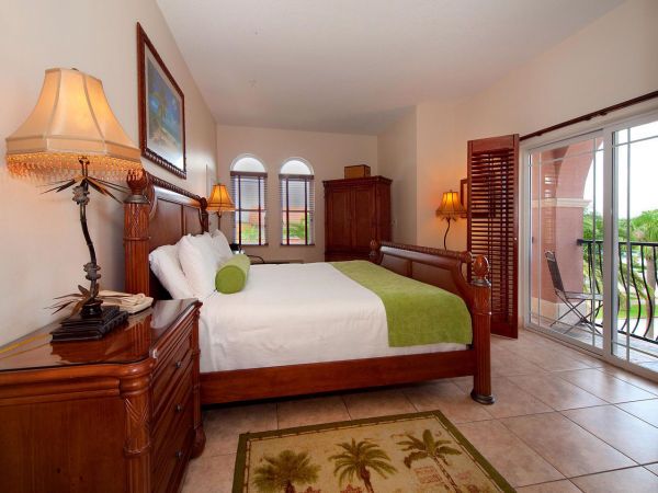 A furnished bedroom with a wooden bed, lamps, an arched window, and a sliding door opening to a patio.
